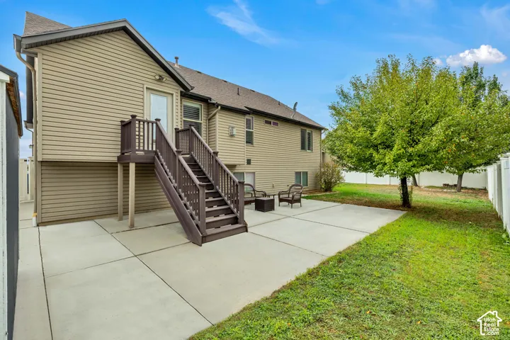Exterior features include horizontal siding, a concrete patio, an elevated wood staircase with matching railings, and a fenced yard with mature trees