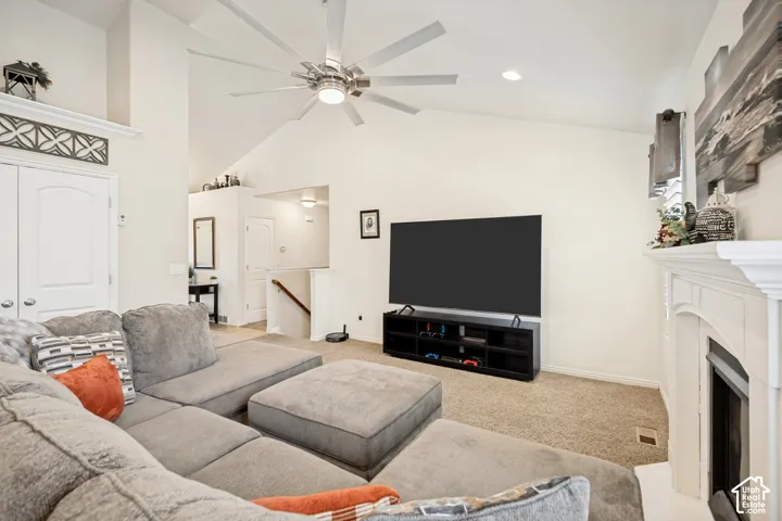 Vaulted ceiling featuring a central multi-blade ceiling fan, arched fireplace mantel with decorative molding, and double-door entry