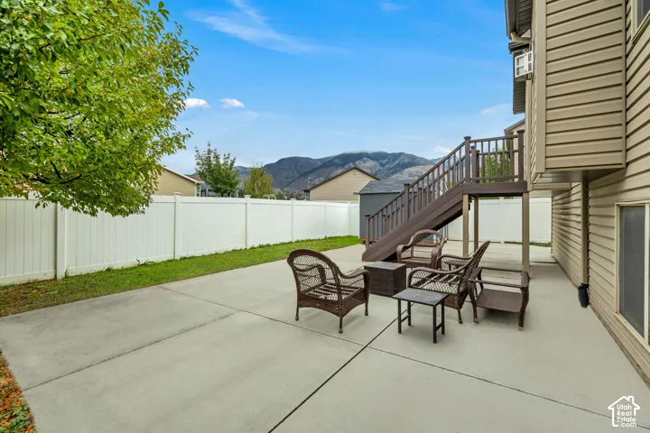 Rear yard featuring a concrete patio, elevated wood-finish deck with stairs, white vinyl privacy fencing, and mountain scenery