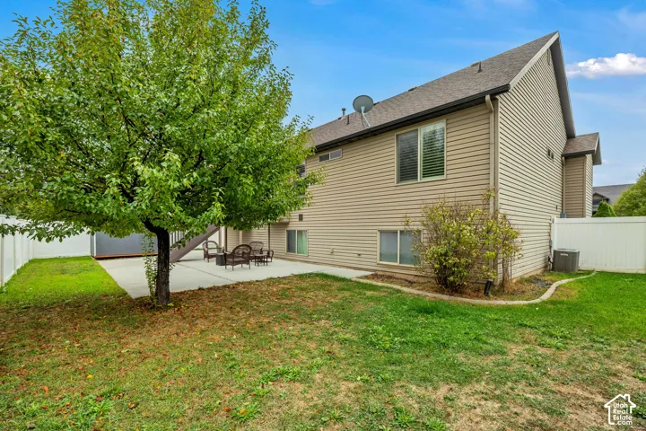 Rear exterior featuring tan vinyl siding, a concrete patio, white vinyl privacy fencing, and a mature tree