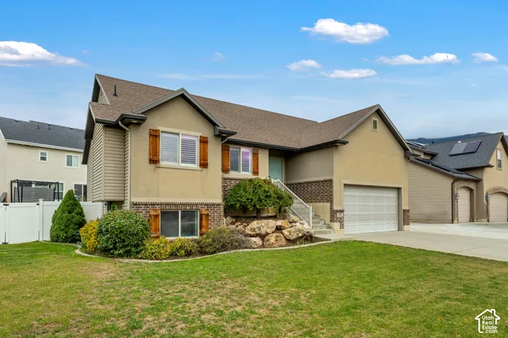 Exterior featuring a stucco and brick facade, attached two-car garage, decorative wood-finish shutters, and landscaped garden with stone boulders