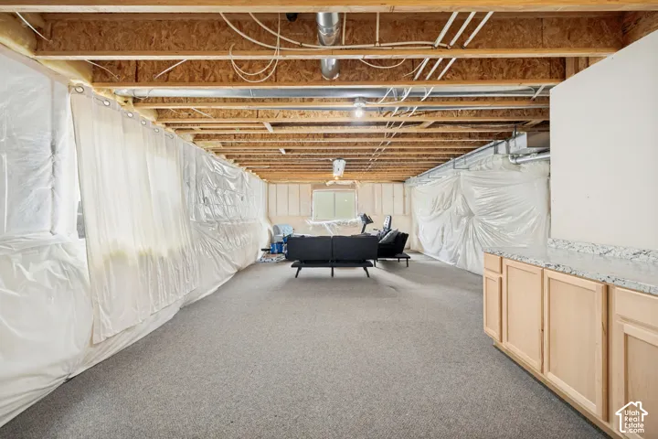 Unfinished lower level featuring exposed wood joist ceilings, wall-to-wall carpeting, and built-in cabinetry with stone-finish countertops