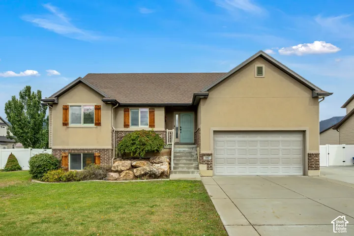 Exterior facade featuring a combination of stucco and brick veneer, decorative wood shutters, a concrete driveway, an attached garage, and landscaped rock garden beds