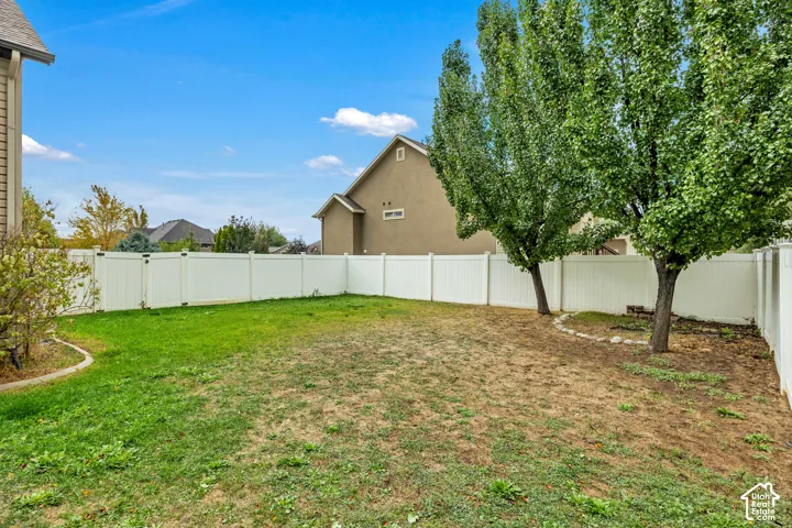 Private backyard enclosed by white vinyl privacy fencing, featuring mature trees and stone border landscaping