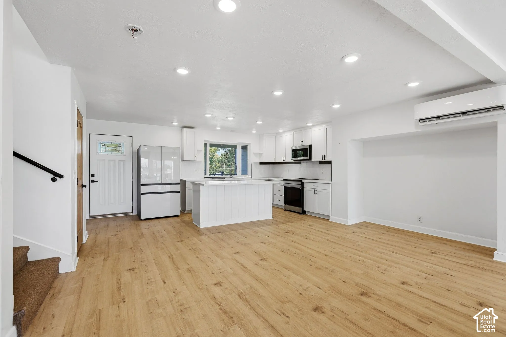 Open-concept living space with wood-finish flooring, recessed lighting, and a white kitchen featuring a large island, white cabinetry, and stainless steel appliances