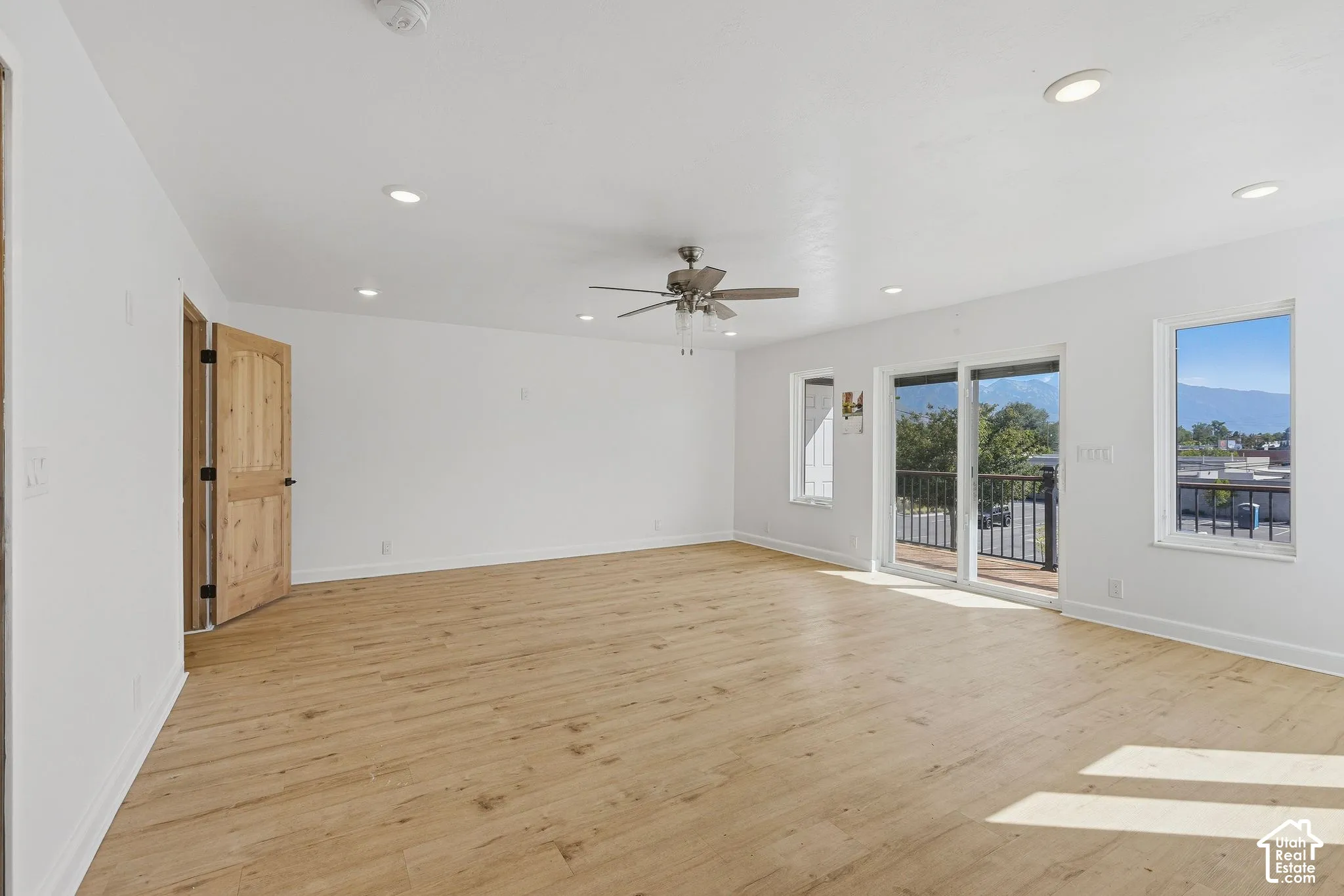 Spacious room featuring wood-finish flooring, recessed lighting, a ceiling fan, and sliding glass door access to an exterior balcony with black railings