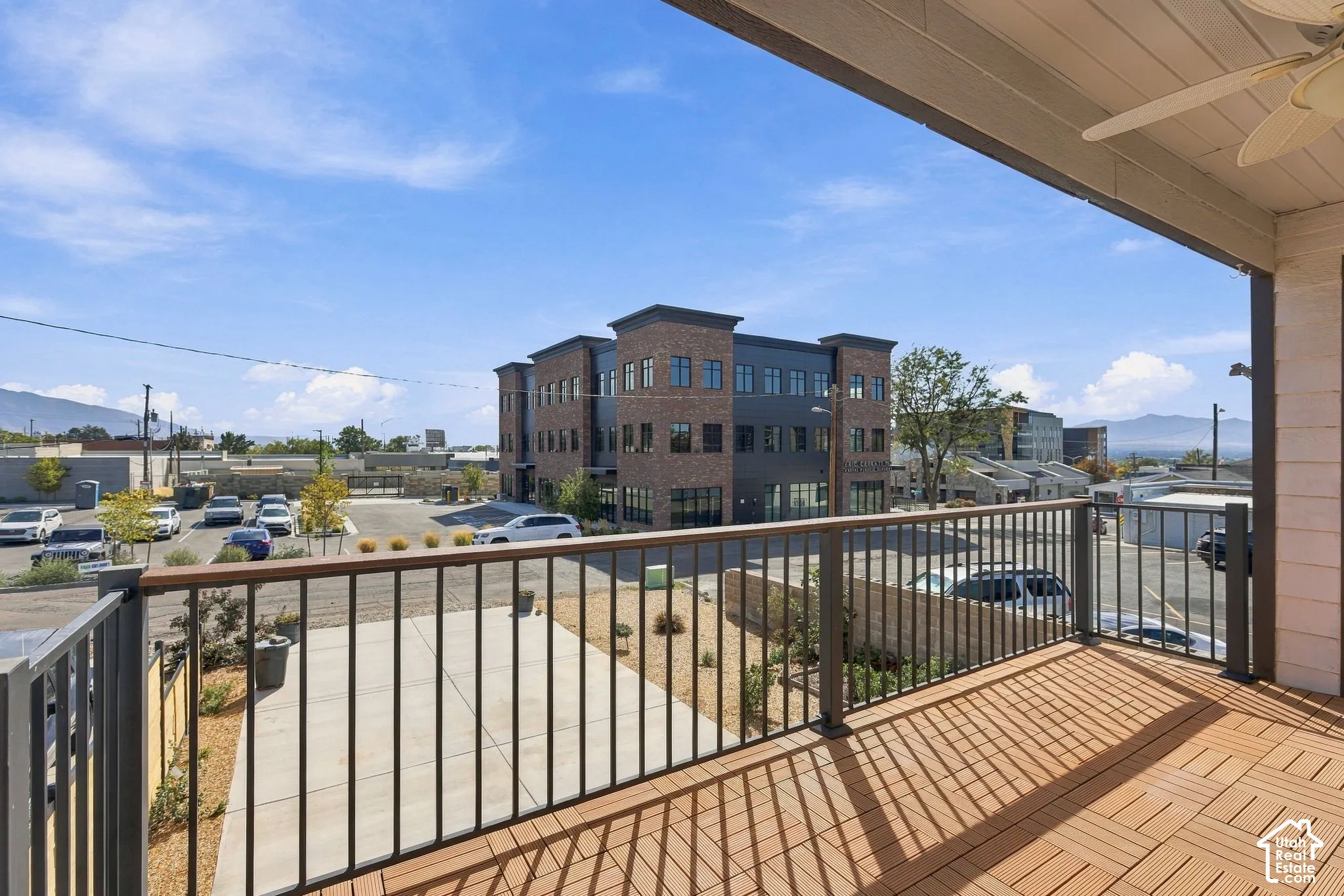 Covered outdoor balcony with wood-finish flooring, metal railing, and an overhead ceiling fan