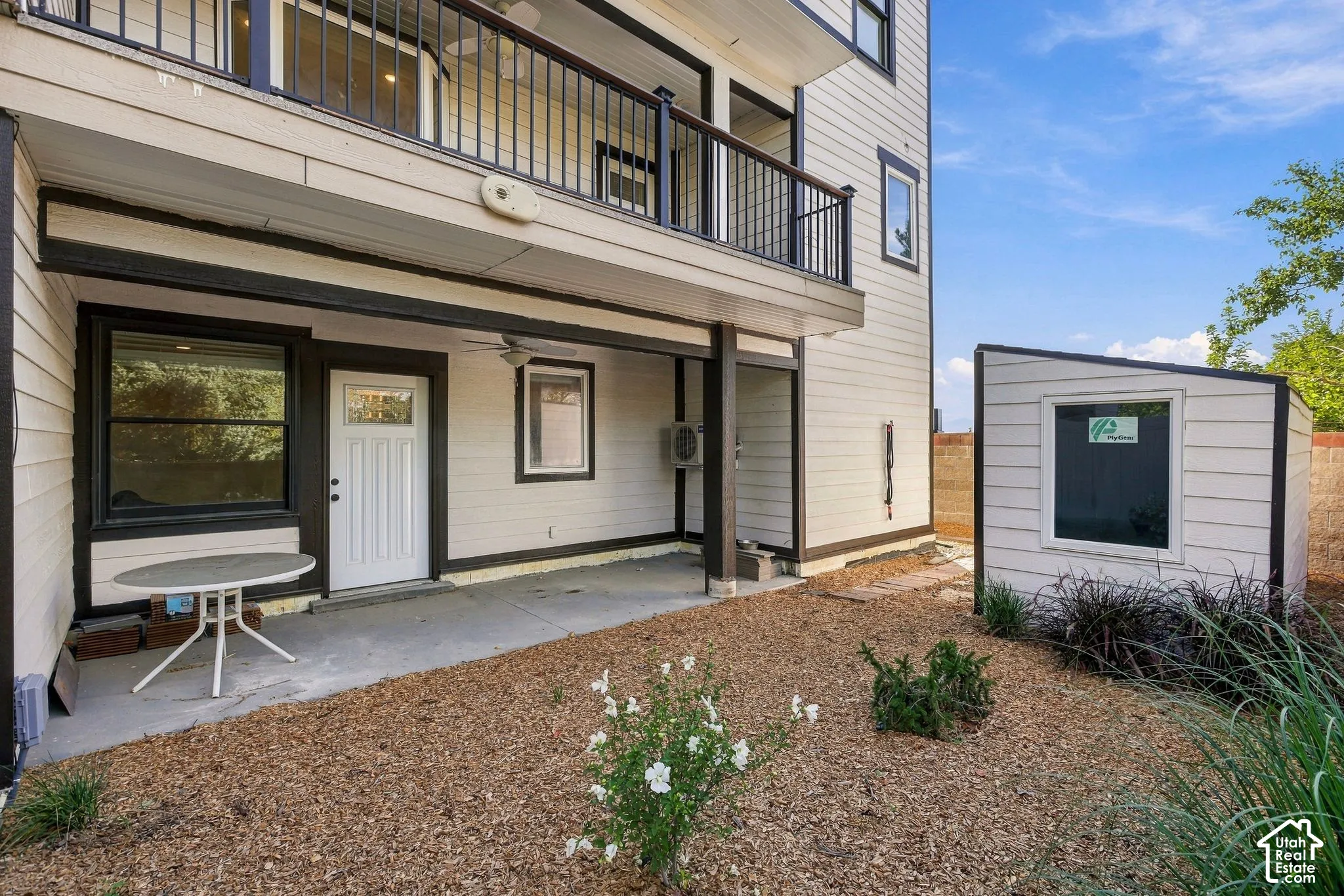 Ground-level patio with overhead balcony, white panel siding, and a detached shed featuring a window