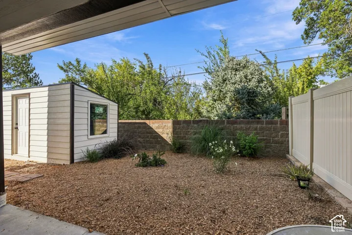 Covered patio space, gravel ground cover, storage shed with window, block retaining wall, and privacy fencing