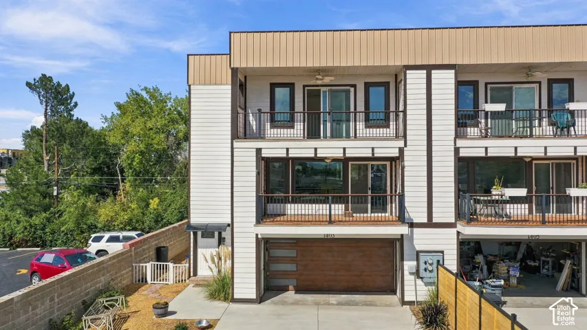 Multi-level townhome featuring a wood-finish garage door, exterior balconies with dark railings, and light siding