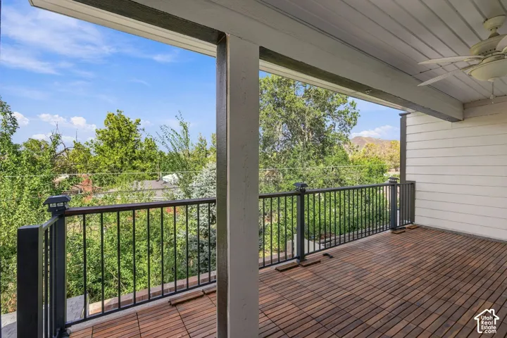 Covered outdoor deck with wood-finish flooring, black metal railing, and a slatted ceiling with a ceiling fan