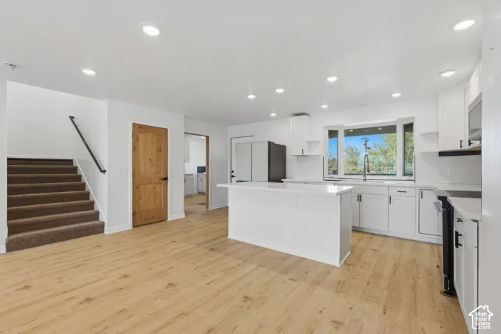 Open-concept kitchen with white shaker cabinetry, an island with shiplap detailing, light wood-finish flooring, and a bay window