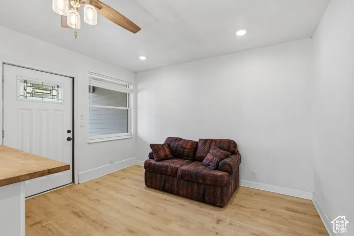 Wood-finish flooring throughout, bright white walls, recessed ceiling lighting, and a window with blinds