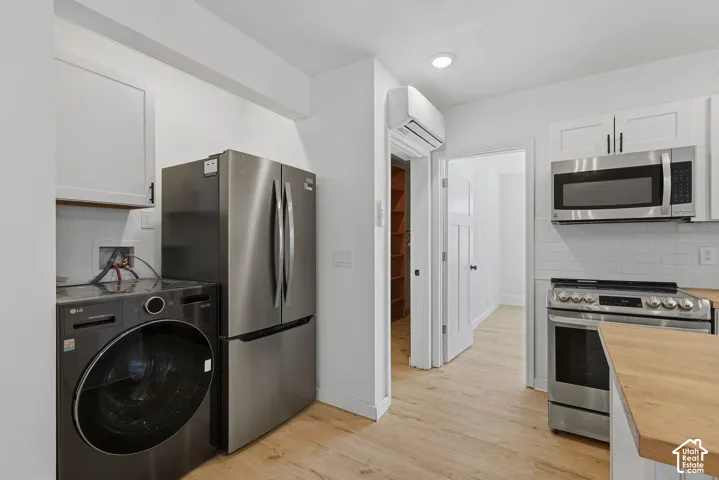 Stainless steel appliances, white subway tile backsplash, wood-finish flooring, white cabinetry, and a mini-split air conditioning unit
