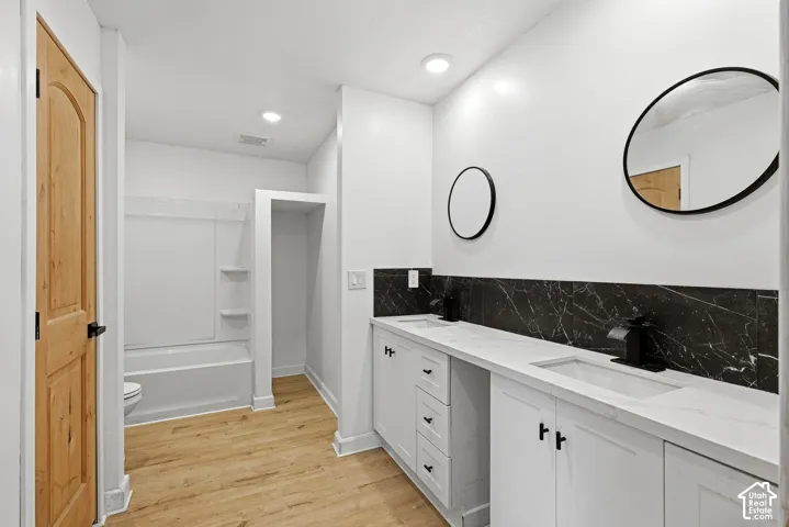 Dual vanity with white cabinetry and integrated sinks, complemented by a black veined backsplash, and wood-finish flooring
