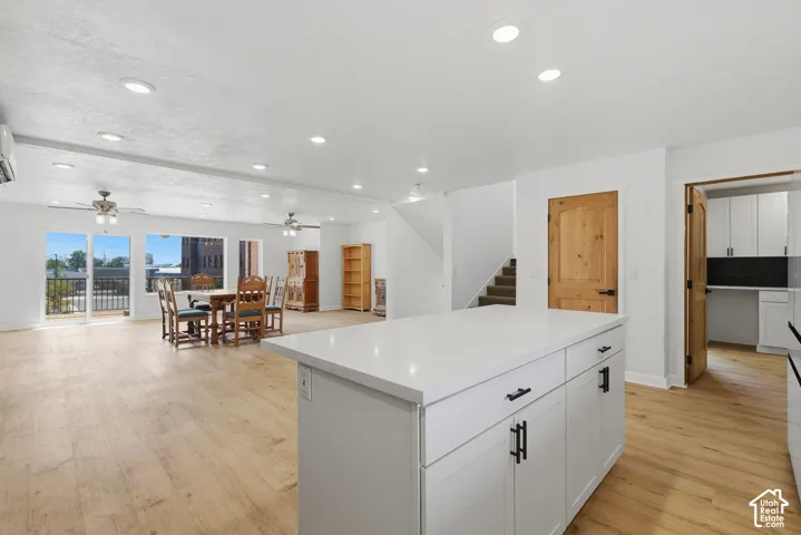 Open-concept living space featuring wood-finish flooring, recessed lighting, and a kitchen island with a light-toned countertop and white cabinetry