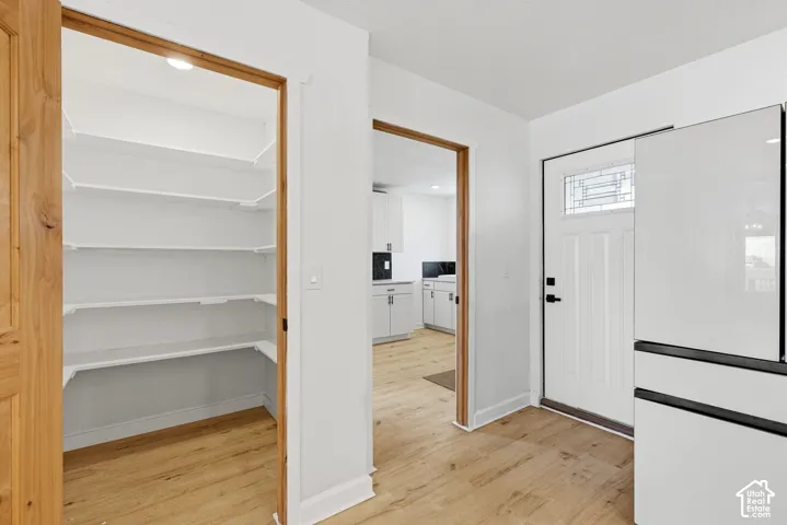 Wood-finish flooring, white paneled door with decorative glass inlay, built-in pantry shelving, and recessed lighting