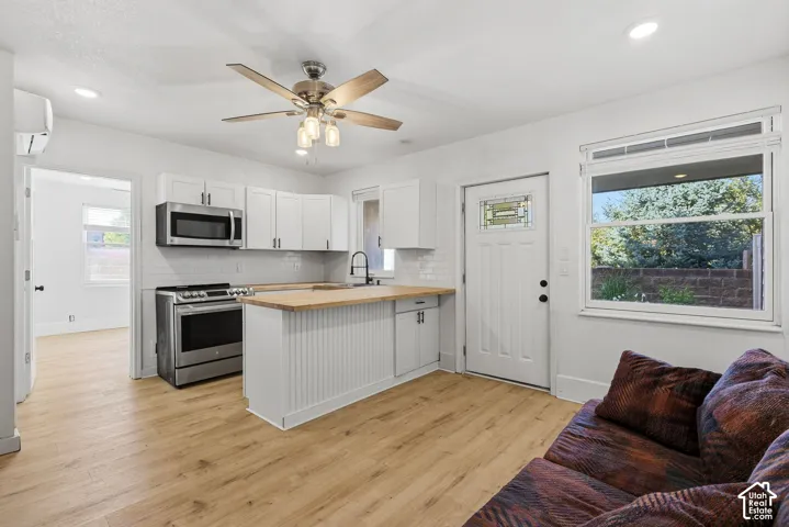 Open-concept living space with wood-finish flooring, white cabinetry, stainless steel appliances, and a butcher block island