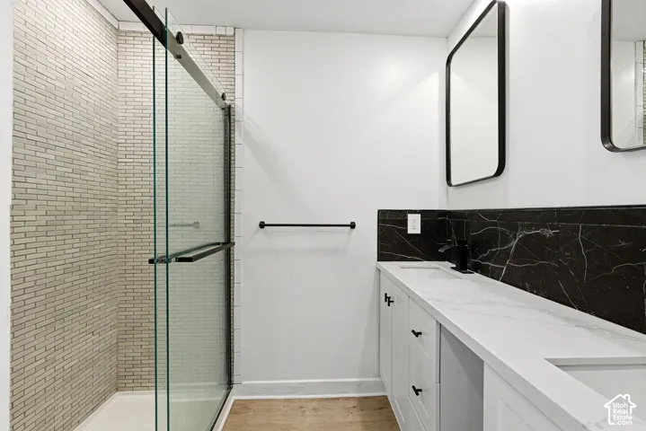 Walk-in shower with subway tile surround, clear glass enclosure, dual vanity with undermount sinks, stone countertops, and black accent tile backsplash