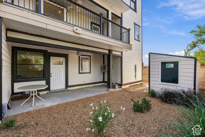 Ground-level patio with overhead balcony, white panel siding, and a detached shed featuring a window