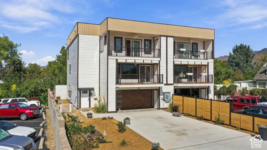 Contemporary multi-level exterior with multiple balconies, wood-finish garage door, and a horizontal slat fence