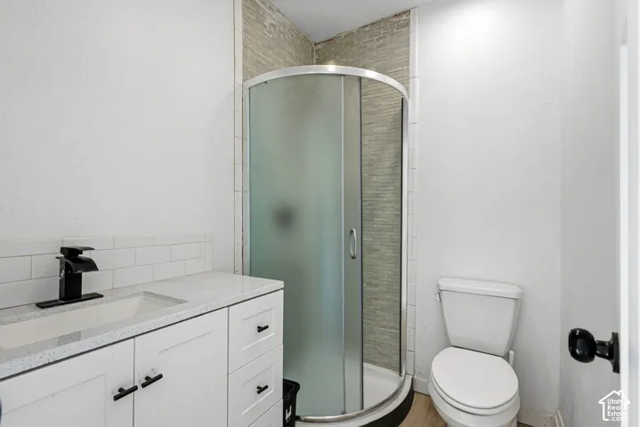 White vanity with integrated sink and matte black faucet, frosted glass shower enclosure, subway tile backsplash, and light wood-finish flooring