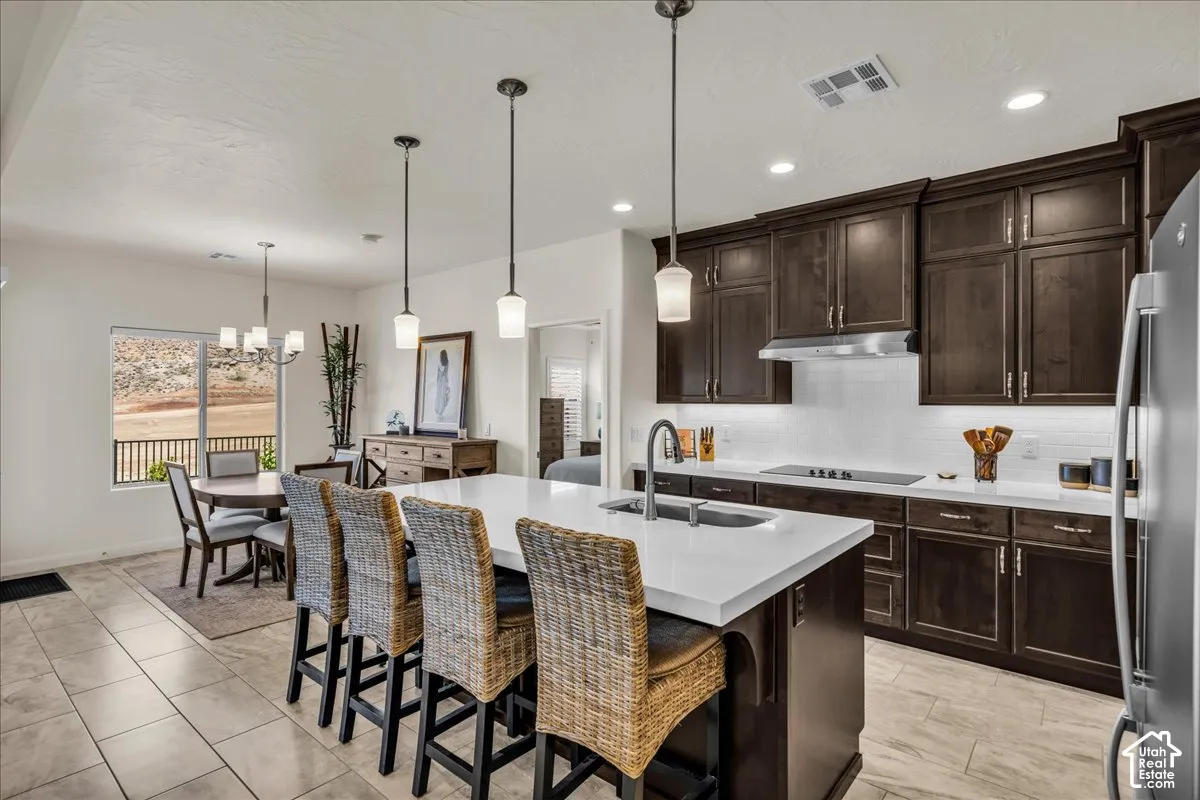 Kitchen featuring dark wood cabinetry, a large central island with white stone-finish countertop, stainless steel undermount sink, pendant lighting, and tile flooring