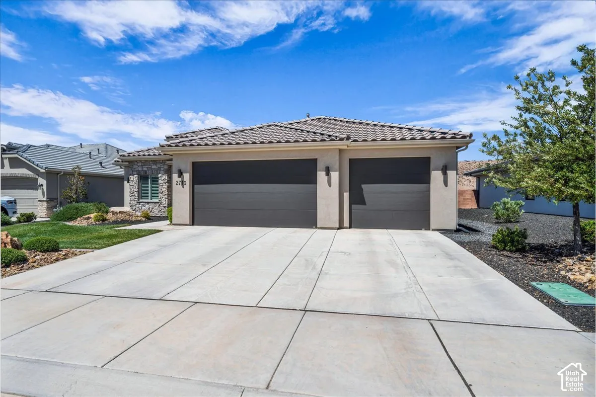Stucco exterior featuring a multi-car garage, stone veneer accent, tile roof, and concrete driveway