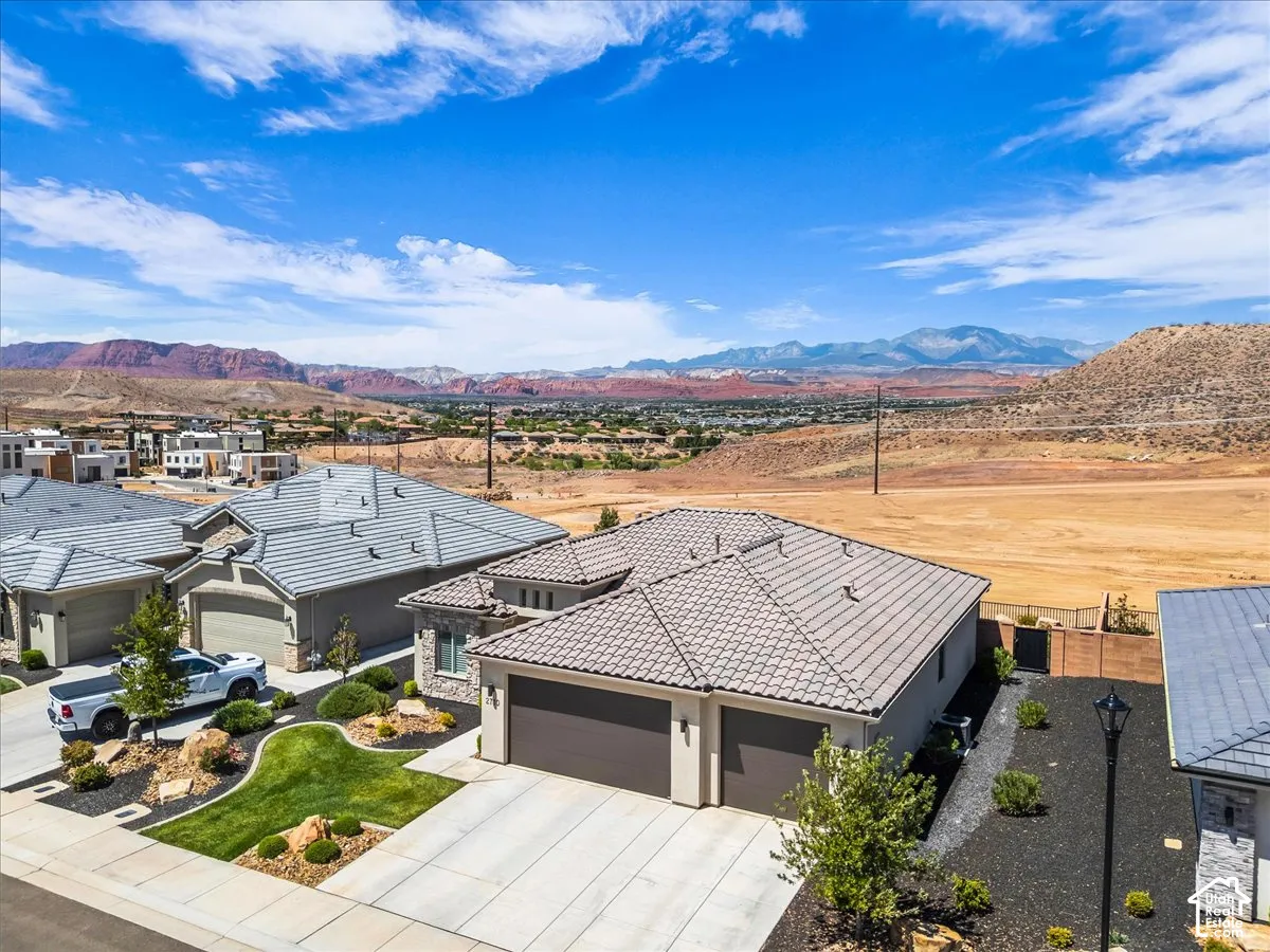 Single-story residence featuring a tile roof, two-car garage, concrete driveway, and professional xeriscape landscaping with mountain and desert scenery