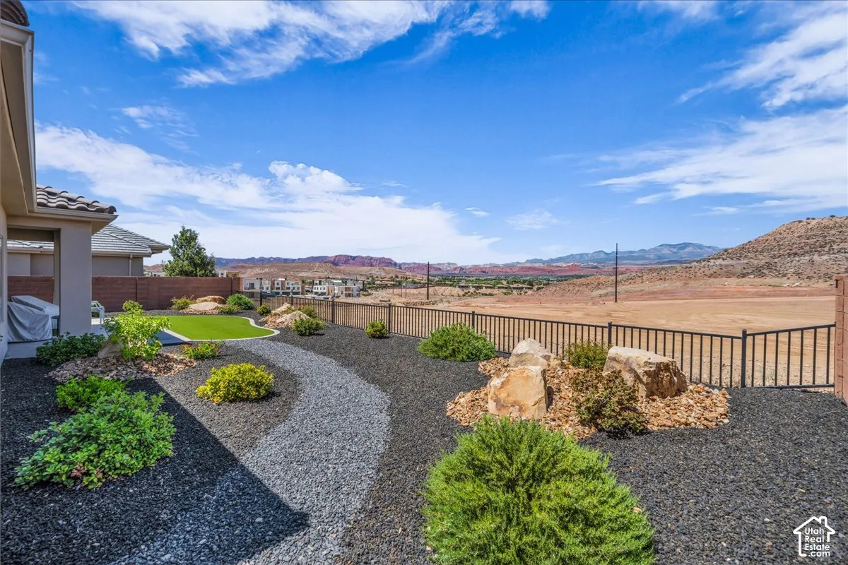 Landscaped backyard featuring black gravel beds, a synthetic lawn section, decorative boulders, and a metal perimeter fence against a mountain backdrop