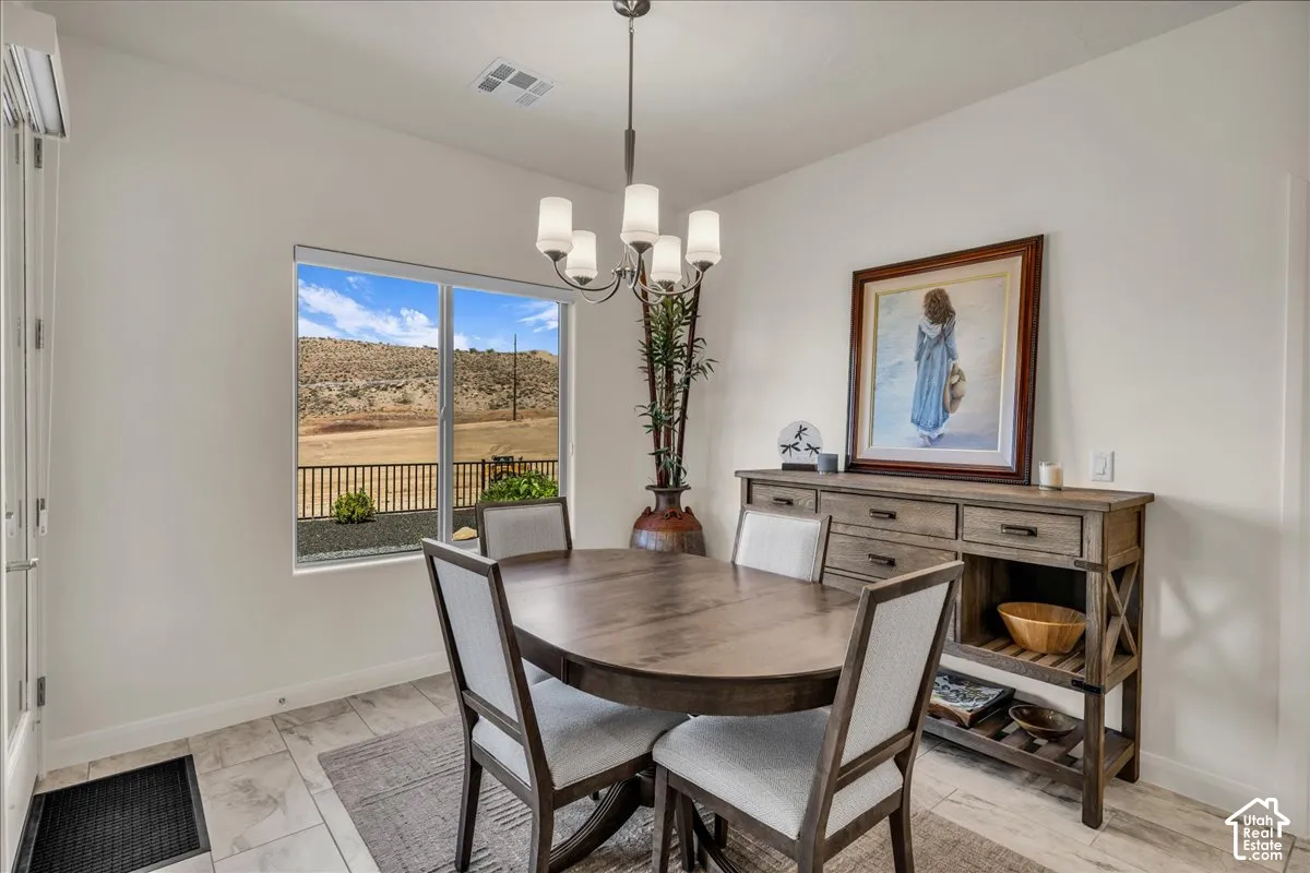 Dining area featuring neutral tile flooring, a multi-light metal chandelier, and a large window displaying desert terrain