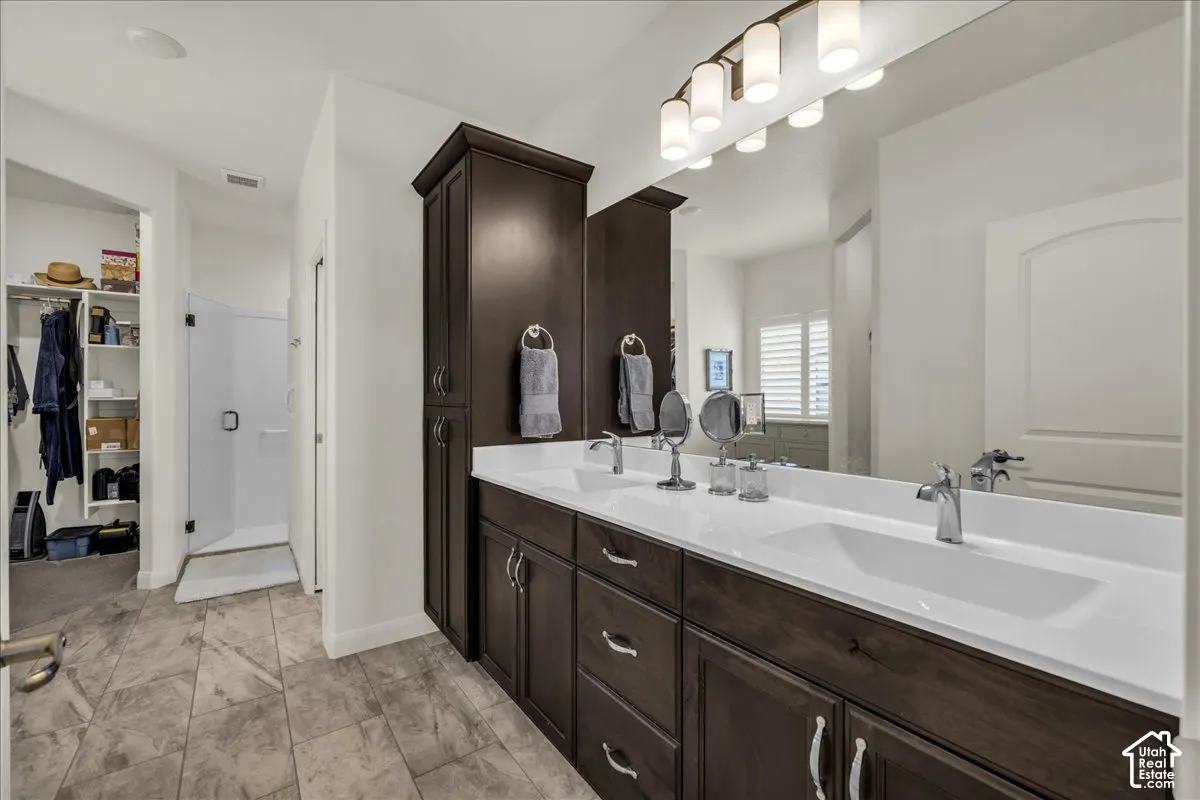 Double vanity featuring dark wood-finish cabinetry, a solid-surface countertop with dual integrated sinks, a full-width vanity mirror, and tile flooring
