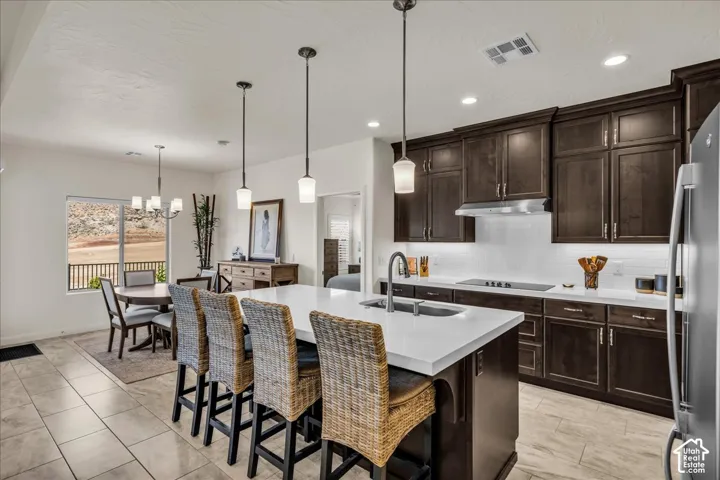 Kitchen featuring dark wood cabinetry, a large central island with white stone-finish countertop, stainless steel undermount sink, pendant lighting, and tile flooring