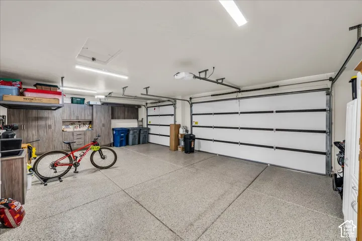 Three-car garage featuring epoxy-coated flooring, built-in cabinetry, overhead LED lighting, and automatic door openers
