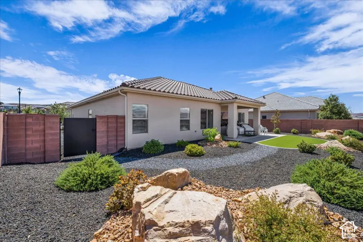 Stucco exterior featuring a tile roof, covered patio, artificial turf lawn, decorative rock landscaping, and a masonry perimeter wall