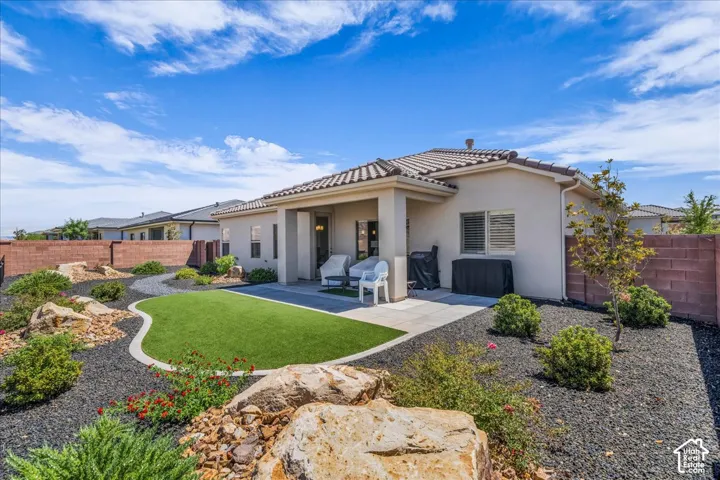 Rear exterior featuring a covered patio, synthetic turf lawn, stone rockscape, and a masonry perimeter wall