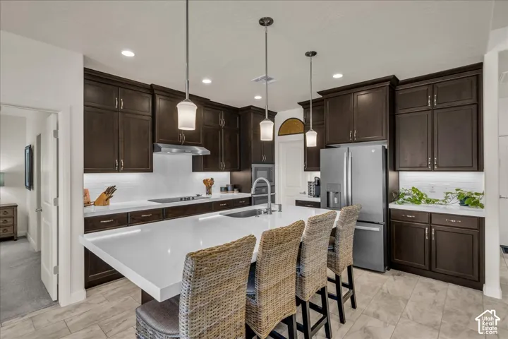 Kitchen featuring dark cabinetry, expansive white countertops, a center island with under-mount stainless steel sink, tile flooring, and recessed lighting