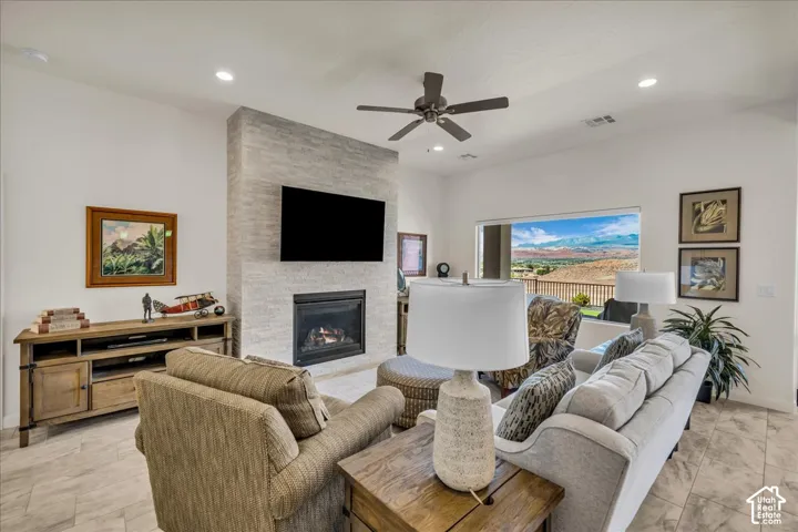 Spacious living room featuring a linear gas fireplace with stacked stone surround, wall-mounted flat-screen television, ceiling fan, recessed lighting, and large windows framing scenic landscape views