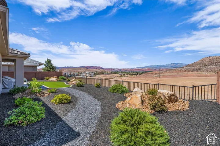 Landscaped backyard featuring black gravel beds, a synthetic lawn section, decorative boulders, and a metal perimeter fence against a mountain backdrop