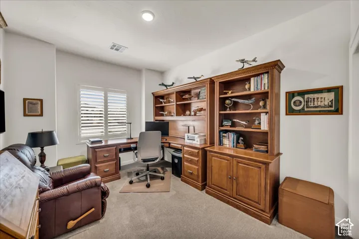 Built-in stained wood shelving and desk unit, carpeted flooring, and window featuring interior shutters