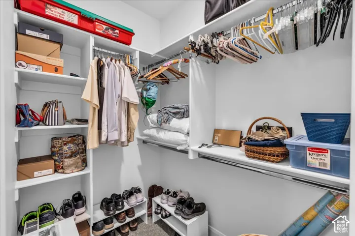 Walk-in closet featuring white built-in shelving, multi-level hanging rods, and neutral carpeting