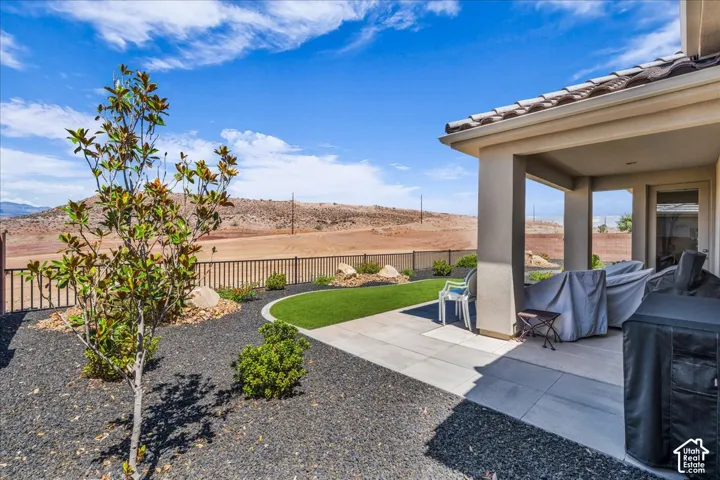 Covered concrete patio with tile-roof overhang, synthetic turf lawn, desert landscaping with decorative rock, and metal perimeter fencing