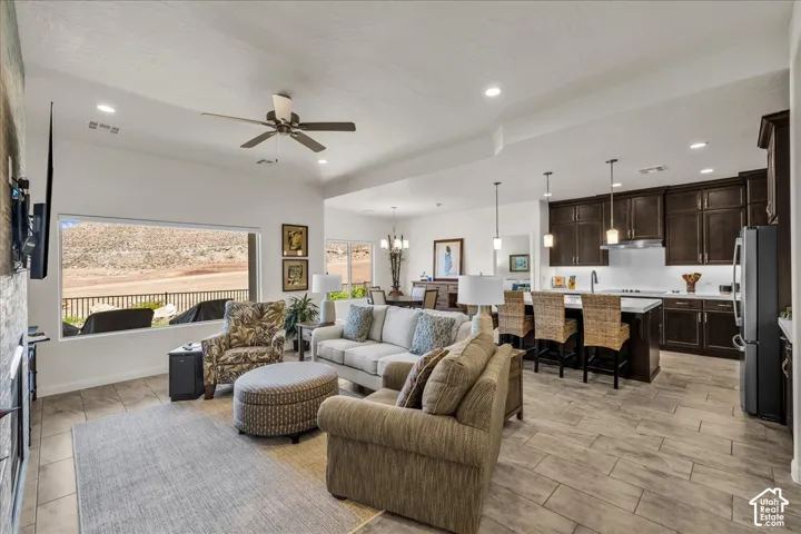 Open-concept living space featuring wood-finish tile flooring, recessed lighting, dark wood cabinetry, a central kitchen island with seating, and a large picture window highlighting a desert landscape
