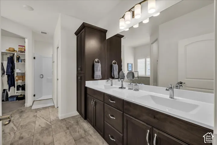 Double vanity featuring dark wood-finish cabinetry, a solid-surface countertop with dual integrated sinks, a full-width vanity mirror, and tile flooring