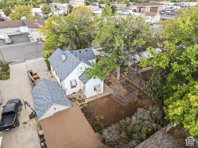 Aerial perspective of a detached residential structure featuring a shingled roof, concrete driveway, and private yard with mature trees