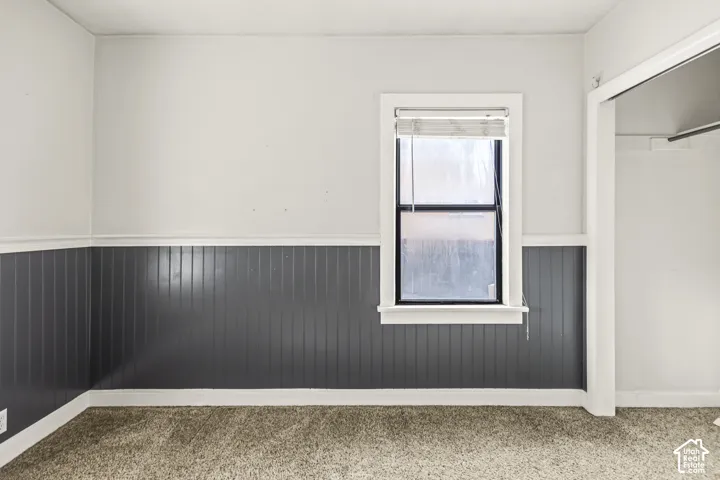 Room featuring grey beadboard wainscoting, a central window with white trim, carpeting, and a built-in closet