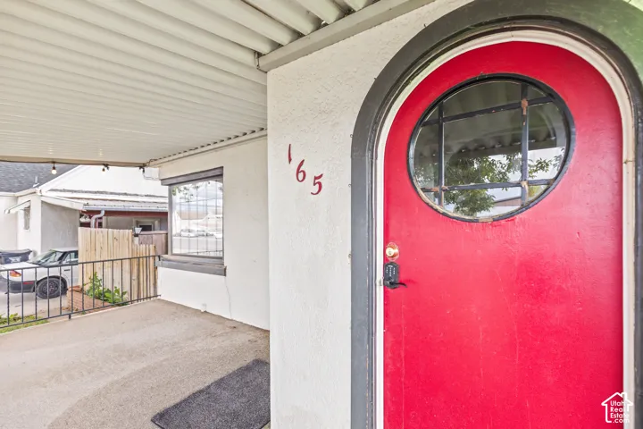 Covered entryway featuring a red arched door with a circular window, decorative trim, and stucco exterior finish