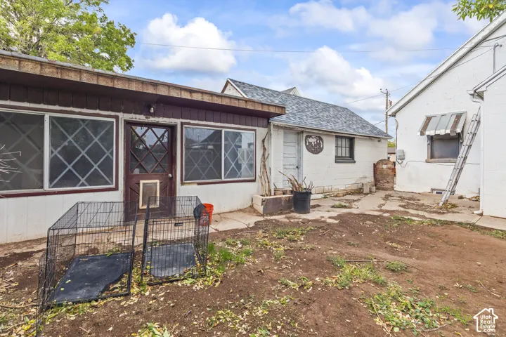 Exterior area featuring white-painted masonry walls, large multi-pane windows, a dark wood-finish entry door with diamond-pattern detailing, and an extensive stone-paver patio