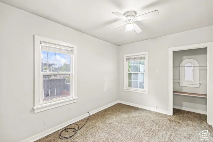 Room featuring wall-to-wall carpeting, dual windows with white casing, a white ceiling fan, and a built-in closet with an arched detail