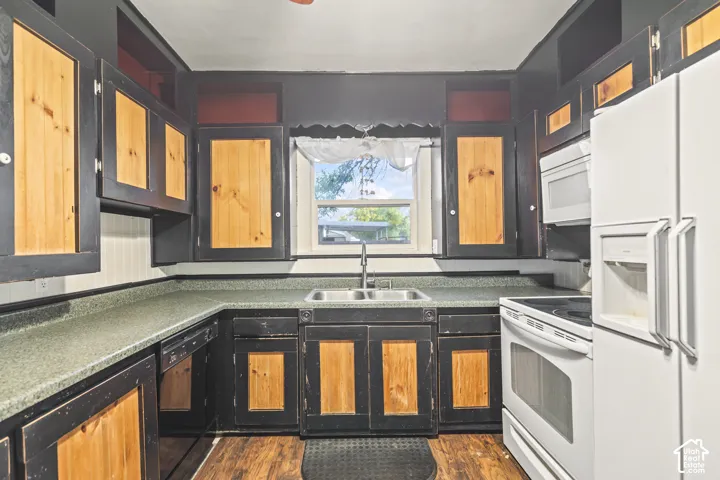 Kitchen featuring two-tone cabinetry with wood-finish center panels, laminate countertops, a double-basin stainless steel sink with a high-arch faucet, and wood-finish flooring